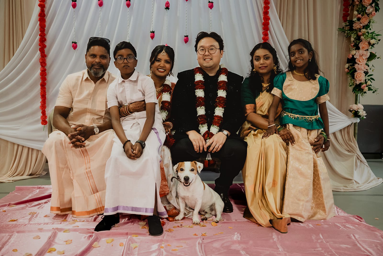 Un amour à six… et à quatre pattes Photo de famille avec les mariés et un chien devant un décor de mariage indien