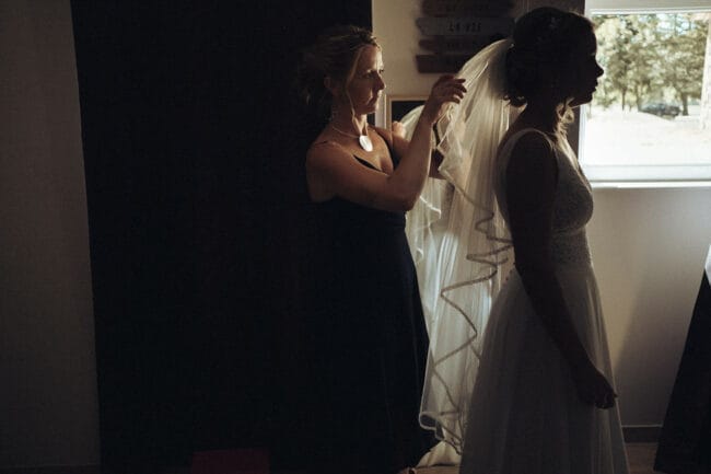 Préparation de la mariée avec l’aide d’une amie, ajustement du voile avant la cérémonie au Domaine de la Pierre