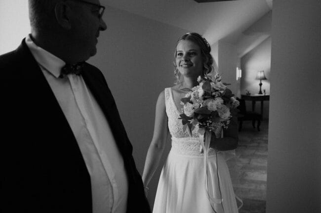 Mariée souriante tenant son bouquet, partageant un moment complice avec son père avant la cérémonie au Domaine de la Pierre