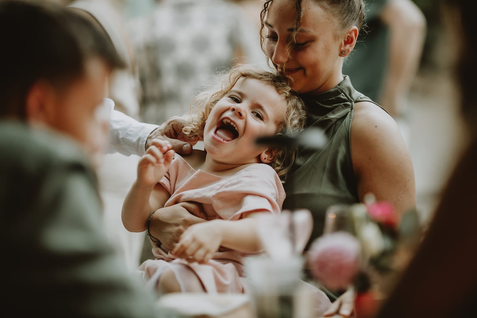 Petite fille riant dans les bras d’une femme, moment de joie et de complicité capturé en lumière naturelle.