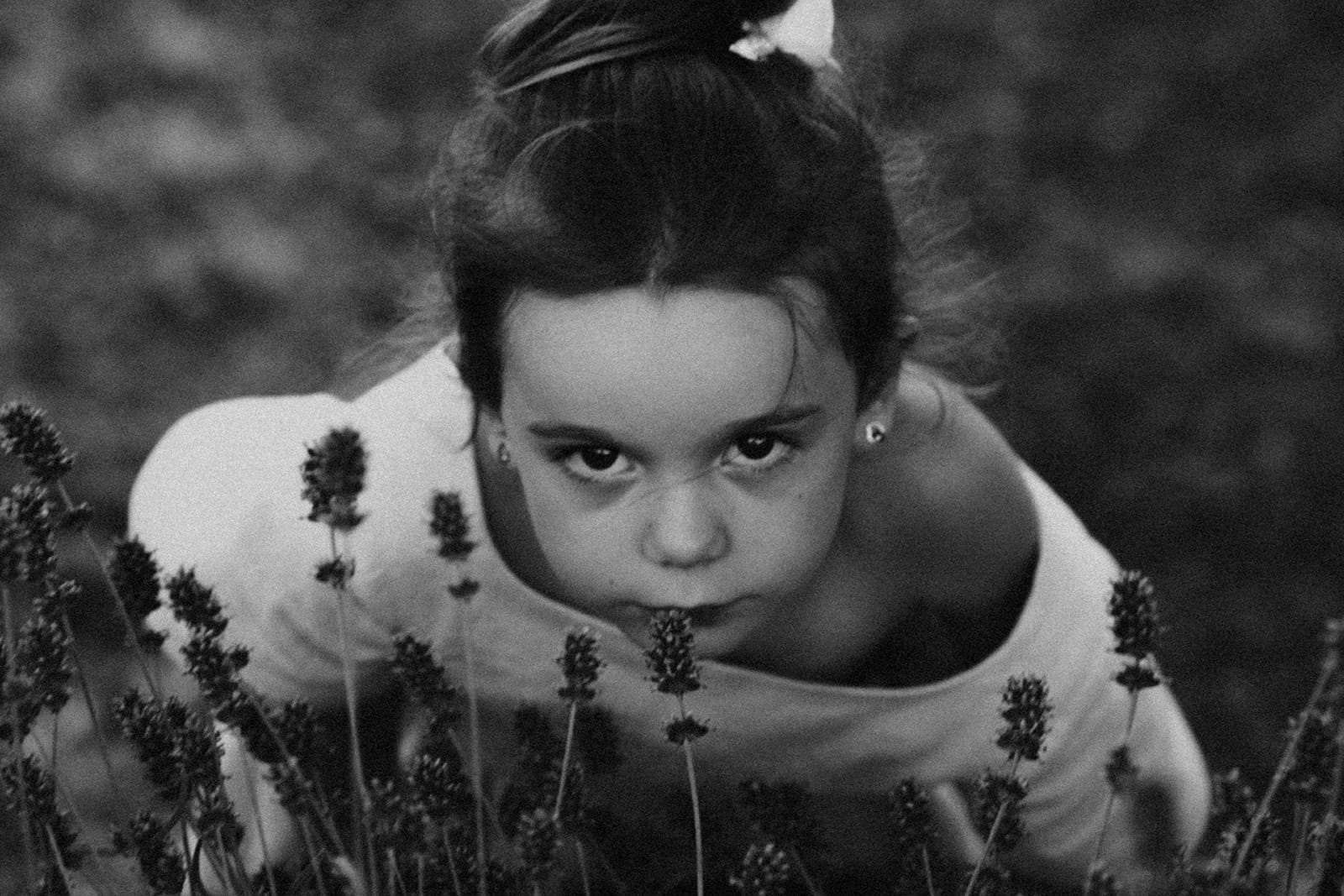 Petite fille observant les fleurs de lavande avec intensité, regard franc et libre, en noir et blanc.