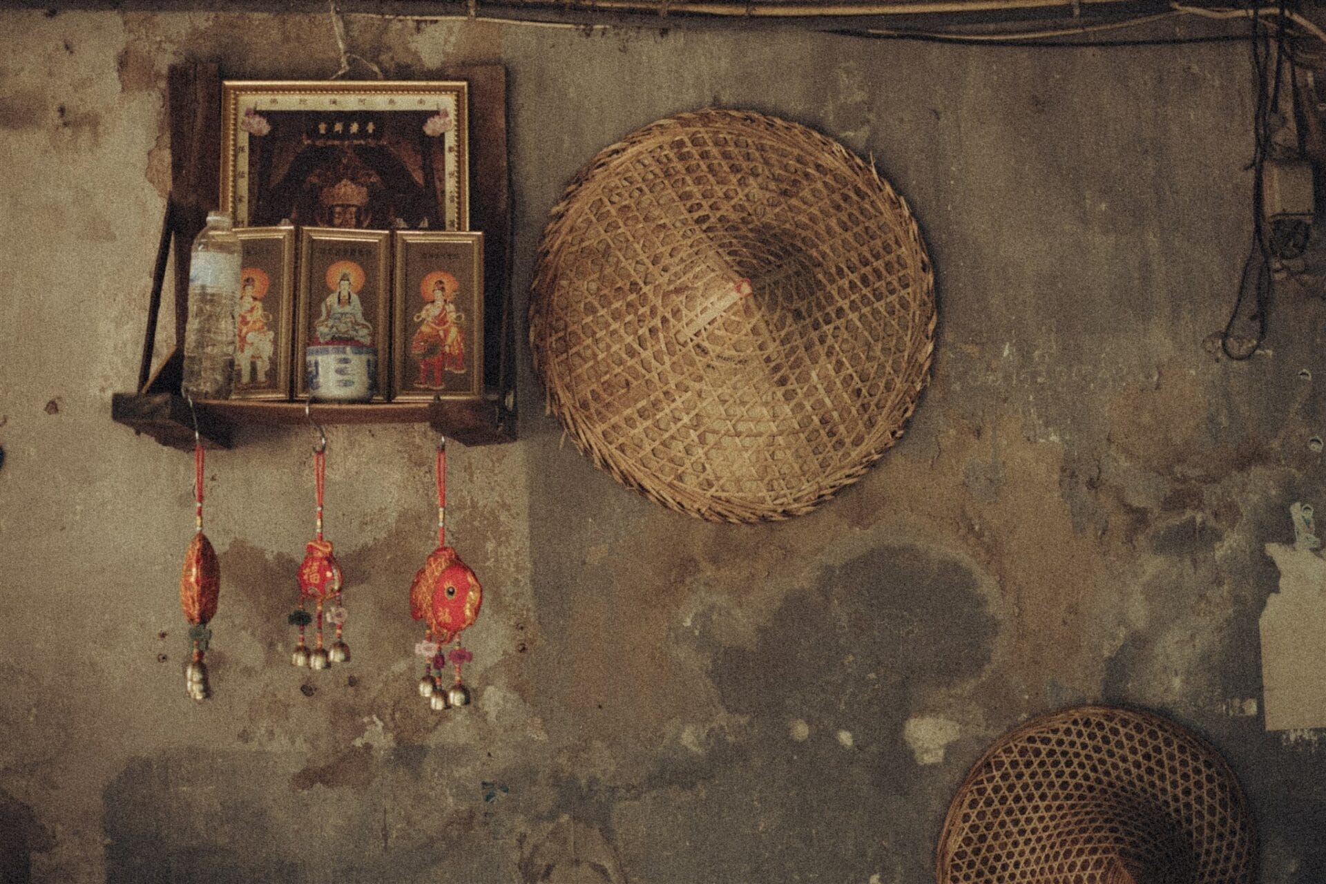 Mur ancien décoré d’icônes asiatiques, d’amulettes rouges suspendues et de paniers en osier.