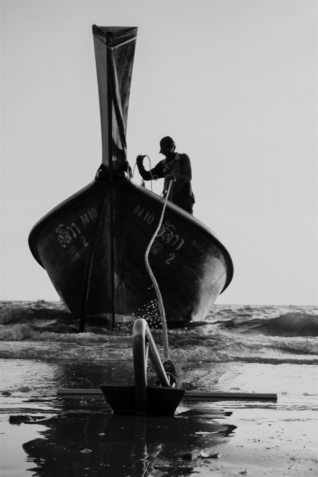 Silhouette d’un homme sur un bateau thaïlandais traditionnel, photographié en noir et blanc au bord de la mer.