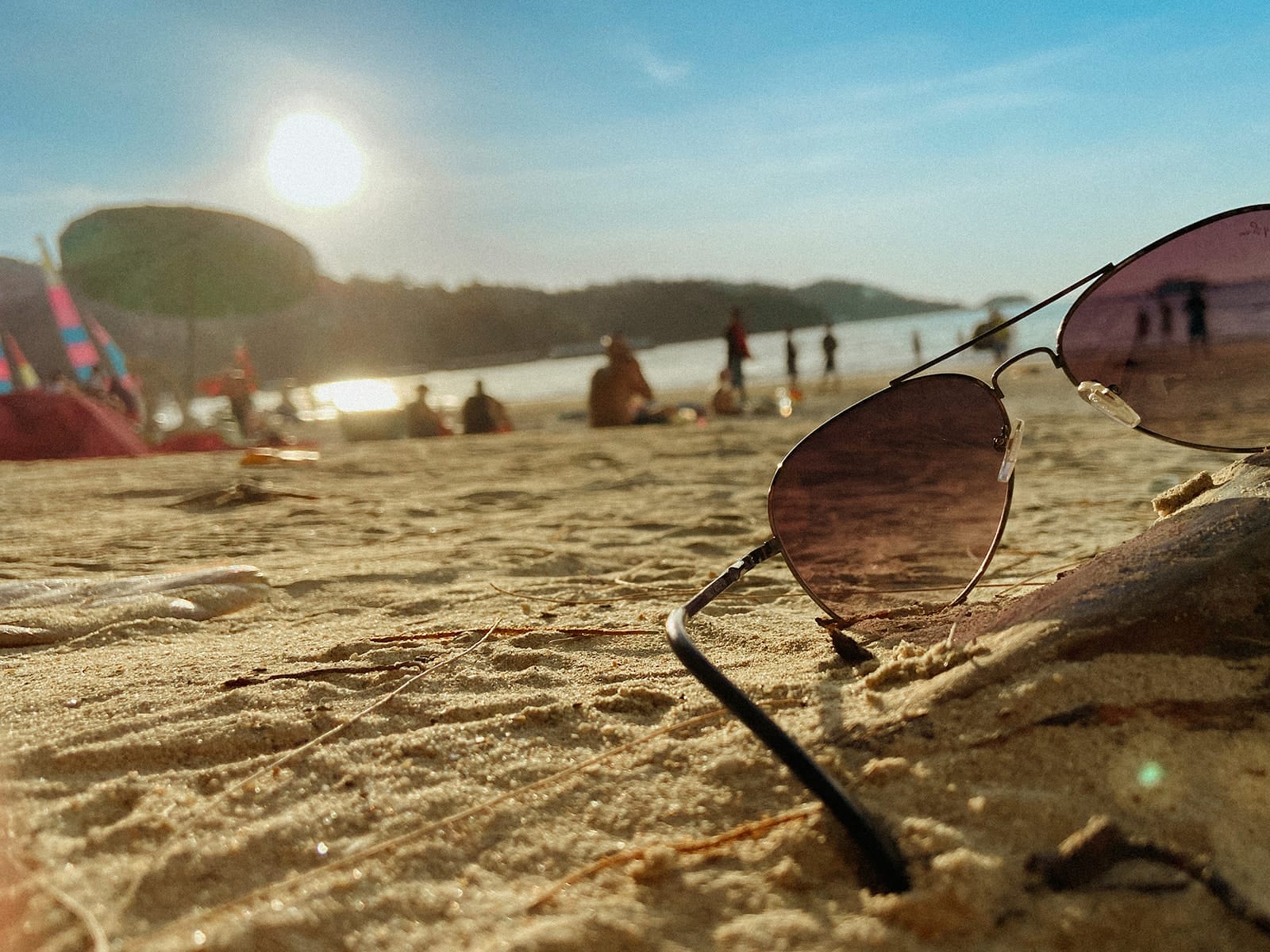Lunettes de soleil posées sur le sable doré d’une plage au coucher du soleil, ambiance tropicale et détendue.